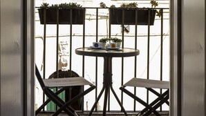 Vista a través de una puerta que muestra un pequeño espacio exterior con dos sillas y una mesa, rodeado por una cerca de metal y plantas en macetas.