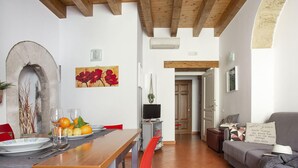 Una sala de estar moderna con techo de madera, un comedor con mesa lista para dos personas y un sofá gris con un cojín.