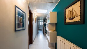 A hallway with a white radiator, a framed picture of a sailboat, and a framed picture on the wall.