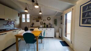 A compact kitchen with a dining area, featuring a wooden table, teal chairs, and pendant lights.