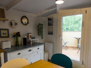 A compact kitchen with a dining area, a window with a view of greenery, and a small outdoor seating area.