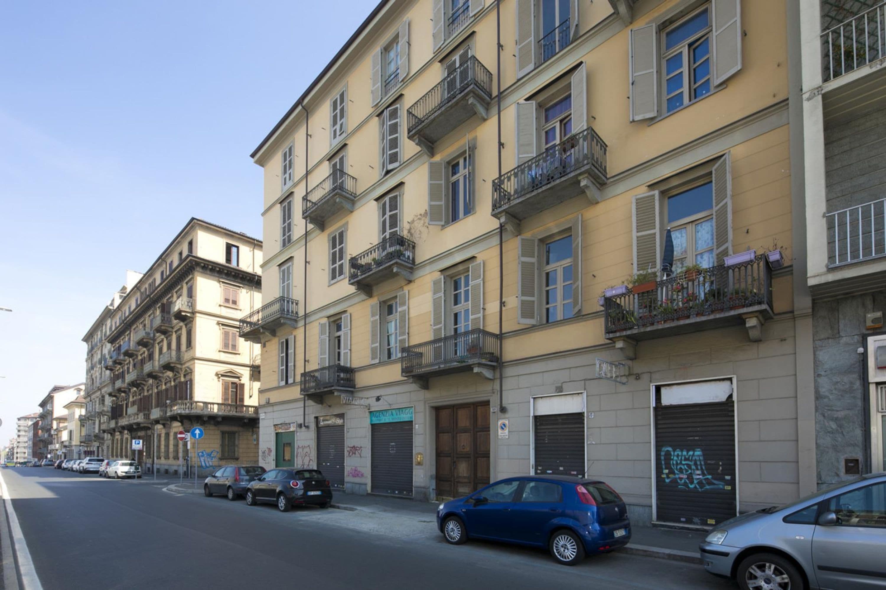 Una vista di strada con edifici a più piani, auto parcheggiate e vetrine di negozi chiuse.
