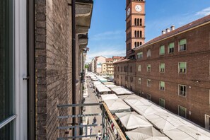 A street view with a clock tower, brick buildings, and outdoor market stalls. - Appartamento nel Cuore di Crocetta by Wonderful Italy (Turin)
