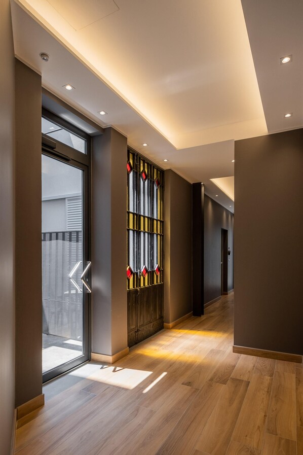 Experience a warm and sophisticated atmosphere in our hotel's minimalist corridor, featuring a large glass door leading to an outdoor area.