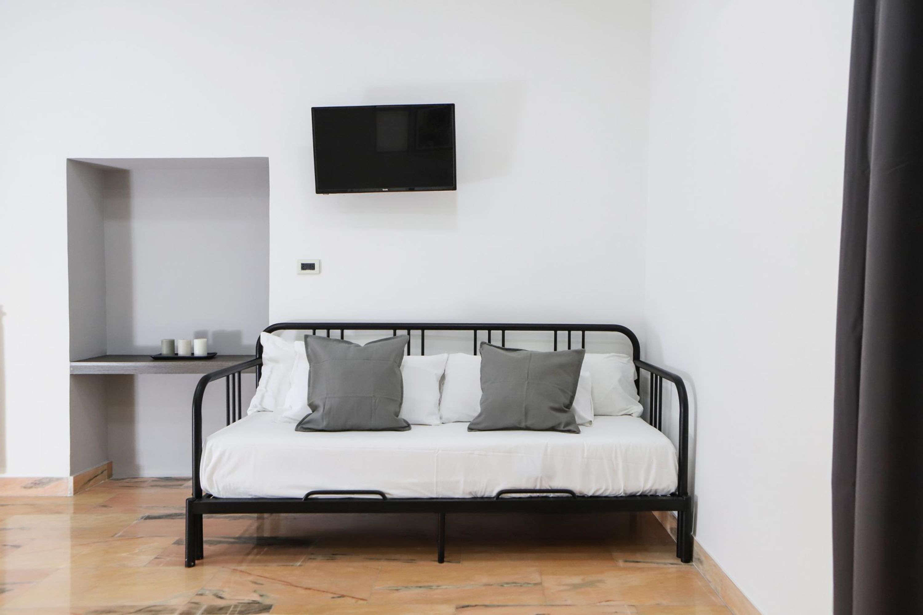 A minimalist room with a bed, a flat-screen TV mounted on the wall, and a small table with cups.