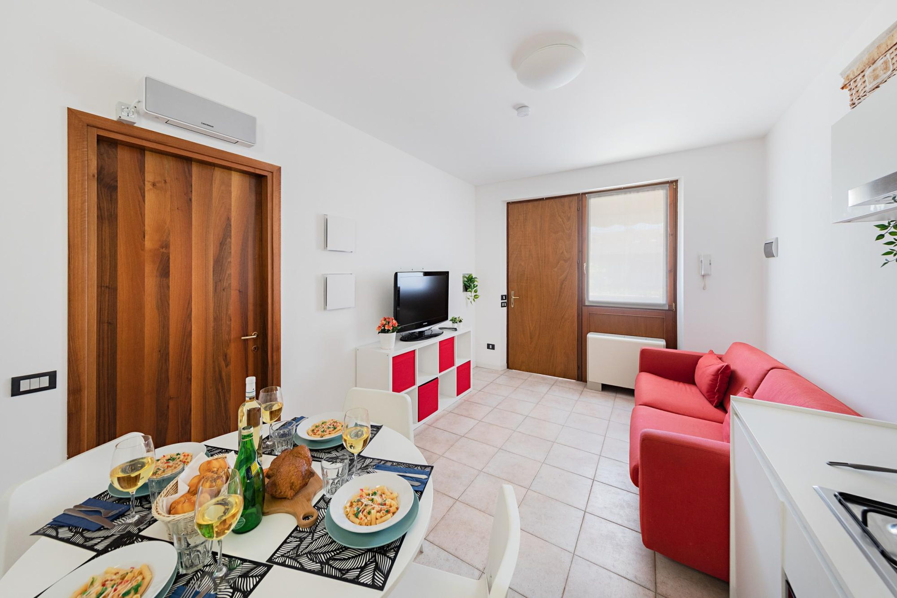 A modern living room with a red sofa, a dining table set with food and drinks, a TV, and a kitchen area.