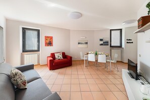 A modern living room with a red sofa, a grey sofa, and a dining area with a table set for four. There are artwork on the walls and a sign that reads "Coffee Bistro".