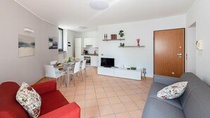 Un salon moderne avec un canapé gris, un fauteuil rouge et un coin repas avec une table mise pour deux personnes.