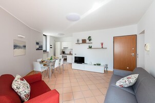 Una sala moderna con un sofá gris, un sillón rojo y una zona de comedor con una mesa dispuesta para dos.
