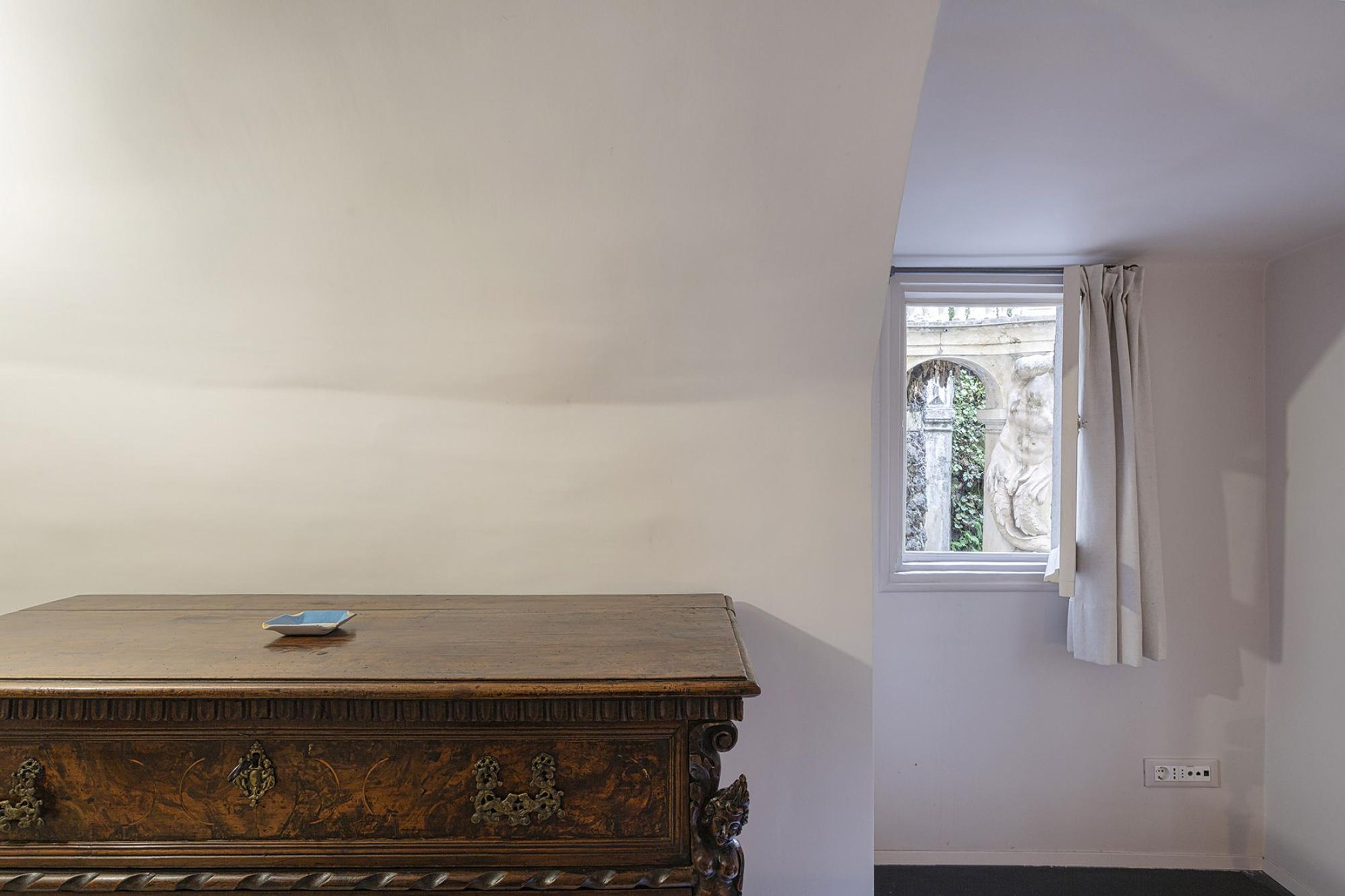 Una habitación con un aparador de madera, un ventanal con cortinas y vistas a un espacio exterior.