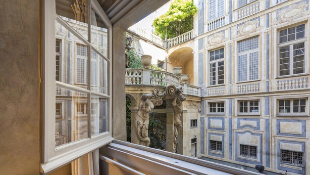Une chambre avec vue sur une cour intérieure agrémentée de balcons richement décorés et d’une statue.