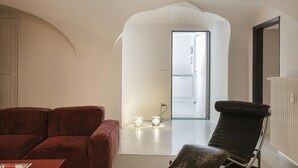 Un salon moderne avec un canapé rouge, un fauteuil noir et une table basse en verre. Une porte donne accès à une autre pièce.