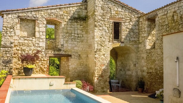 Un edificio de piedra con piscina, arcos y mobiliario exterior.