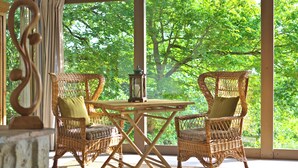 Un espacio de estar al aire libre techado, con sillas de mimbre y una mesa, con vista a un paisaje verde y exuberante.