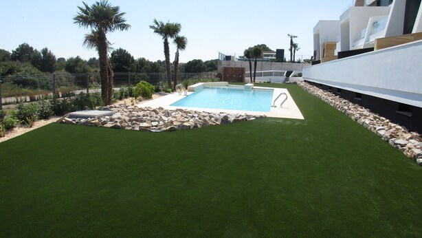 A swimming pool with artificial grass, surrounded by rocks and palm trees.