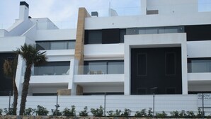 A modern building with multiple balconies, a stone wall in the foreground, and a clear sky.