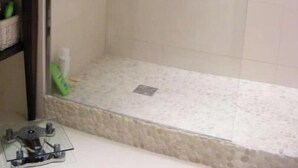 Zona doccia con porta in vetro, soffione metallico e pavimento effetto pietra.