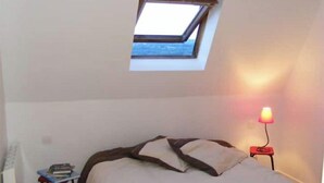 Una camera da letto con un lucernario, un letto, un comodino con dei libri e una lampada rossa.