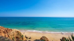 Una platja amb aigua blava cristal·lina, penya-segats rocosos i poques persones a la sorra.
