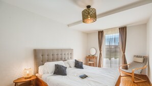 Een slaapkamer met een bed, een stoel, een nachtkastje, een lamp en een raam met gordijnen.