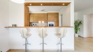Een moderne keuken met houten kastjes, een inbouwoven en een bar met drie witte barkrukken.