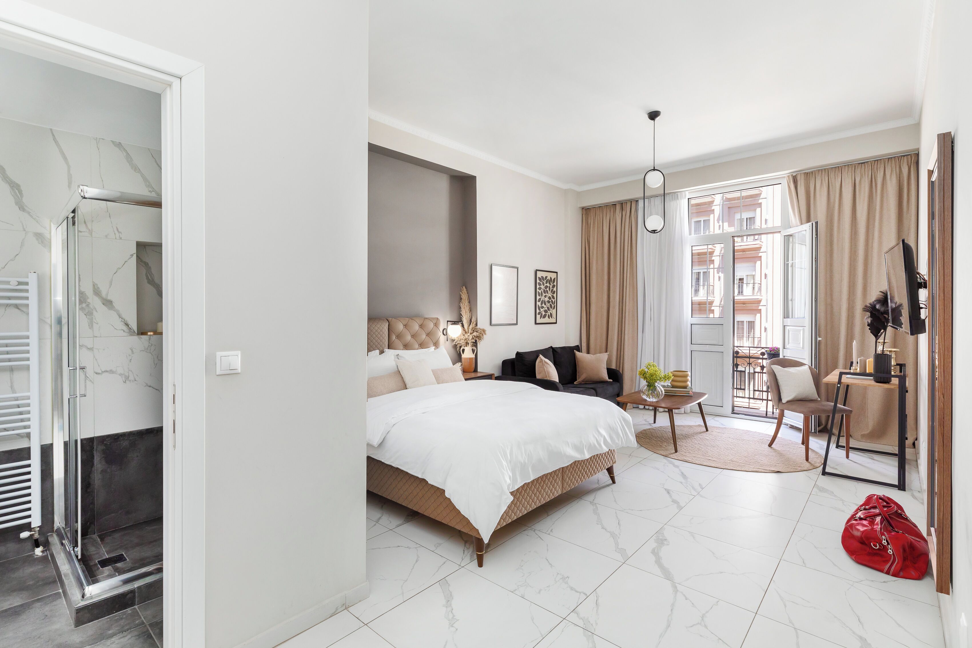 Una habitación de hotel moderna con cama, zona de estar, mesa de comedor y vistas a la ciudad.