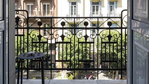 A balcony with a metal railing, a small table, and a view of multi-story buildings in the background. - BLACK ONYX COMFORT SUITES (Thessaloniki)