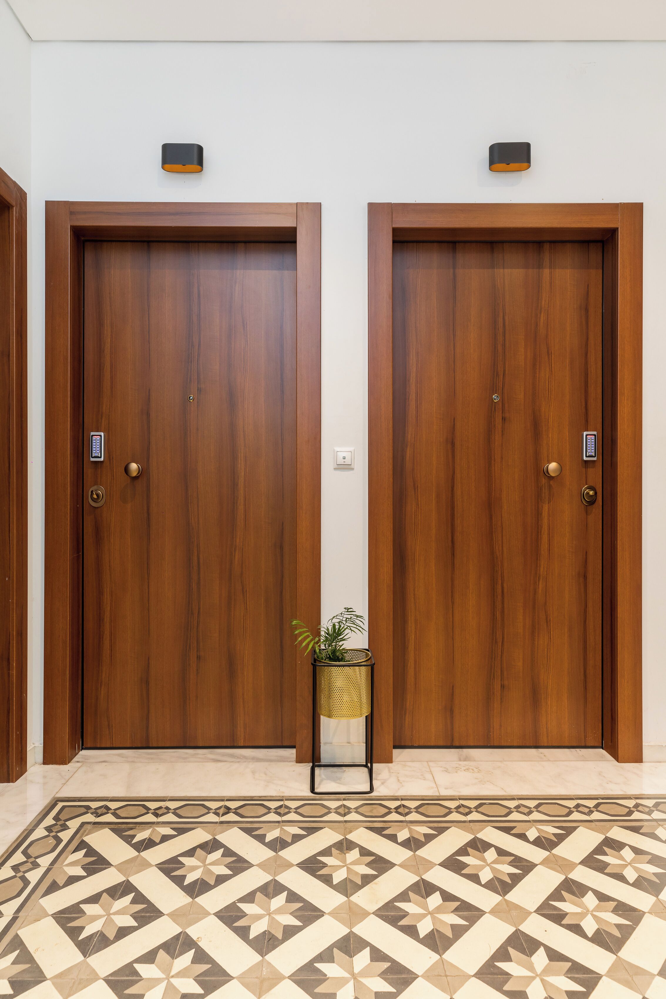 Dos puertas de madera con cerraduras electrónicas y una pequeña planta en maceta entre ellas.