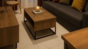A modern living room with a dark sofa, wooden coffee table, and a chair. There is a window with curtains, an air conditioning unit on the wall, and a vase with pampas grass on the floor. - BLACK ONYX COMFORT SUITES (Thessaloniki)