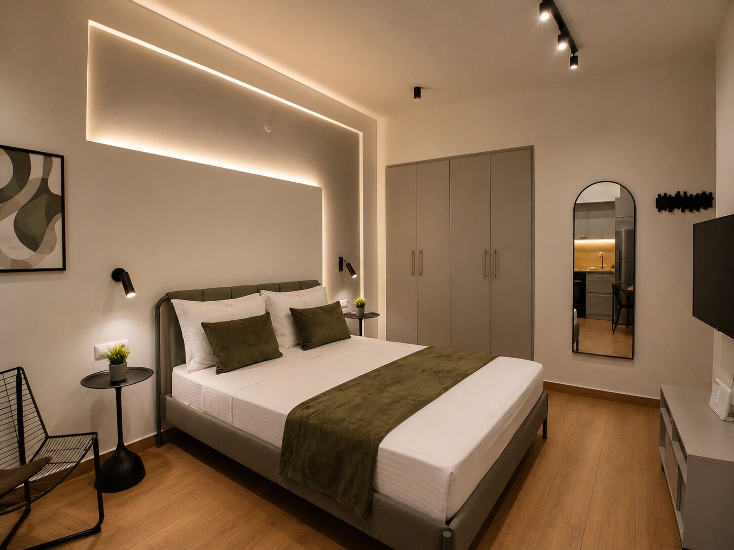 A modern bedroom with a large bed, bedside tables, a wardrobe, a mirror, and a TV.