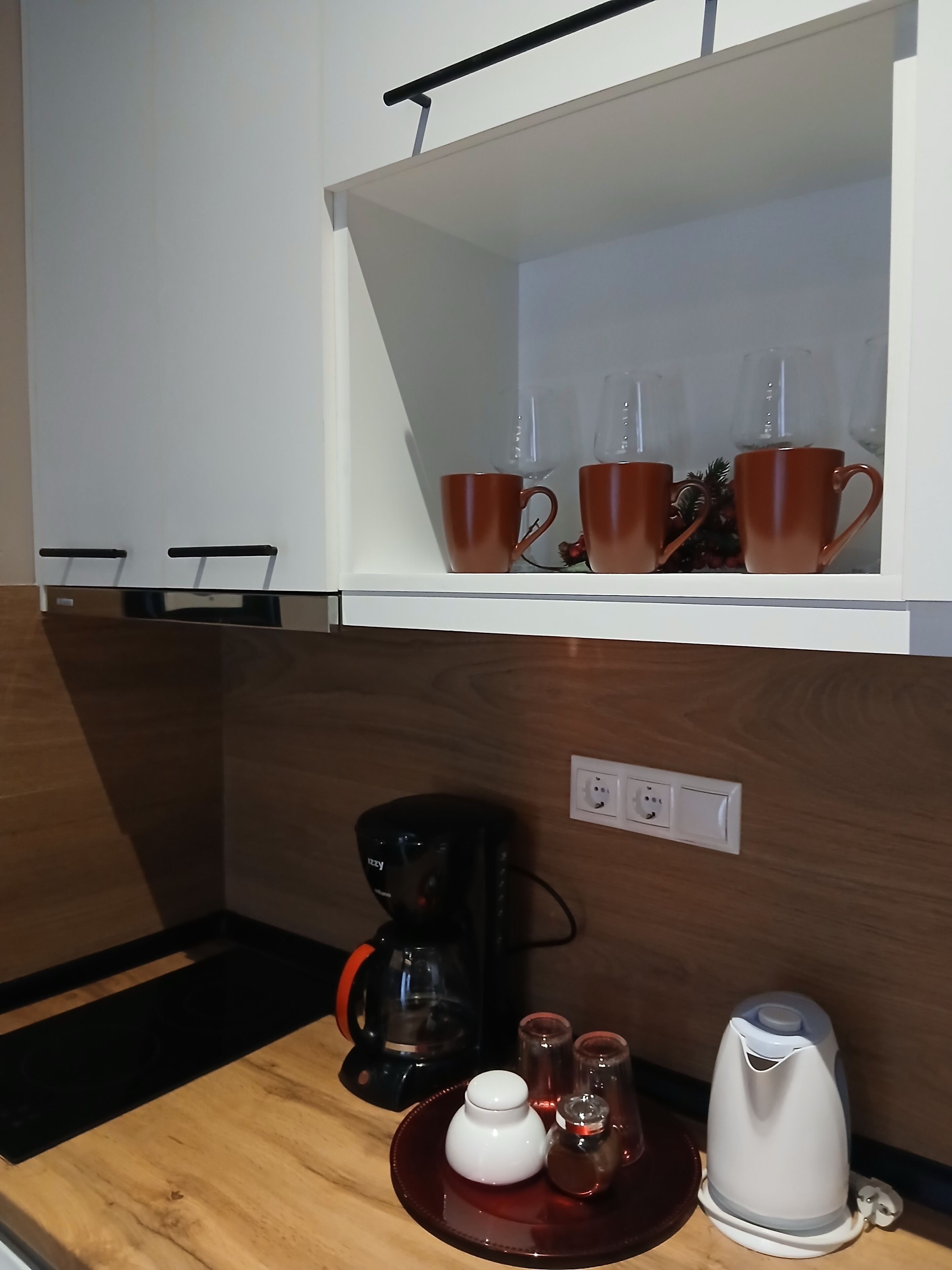 Een keuken met een koffiezetapparaat, een waterkoker en een theeset op het aanrecht.