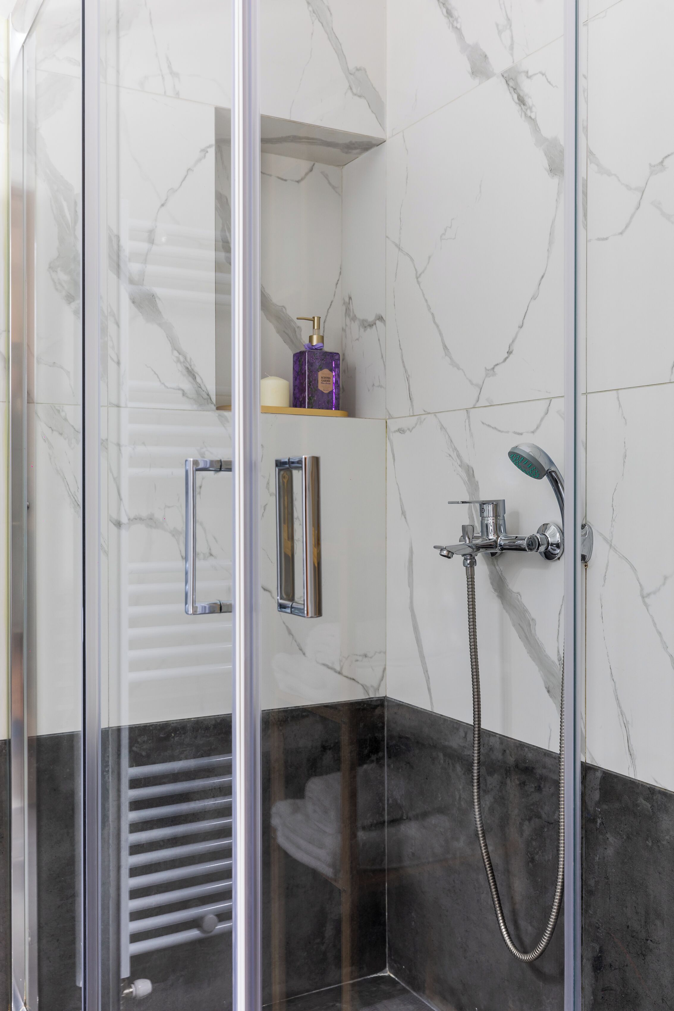 Un baño moderno con cabina de ducha de vidrio, paredes de mármol y suelo de baldosas blanco y negro.