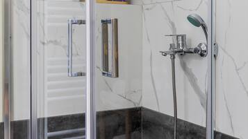 Un baño moderno con cabina de ducha de vidrio, paredes de mármol y suelo de baldosas blanco y negro.