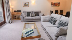 A living room with a grey sofa, a glass coffee table, and a dining area with a table and chairs. - Beechside (Ambleside)