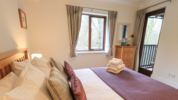 A neatly made bed with pillows, a stack of towels, and a window with curtains. - Beechside (Ambleside)
