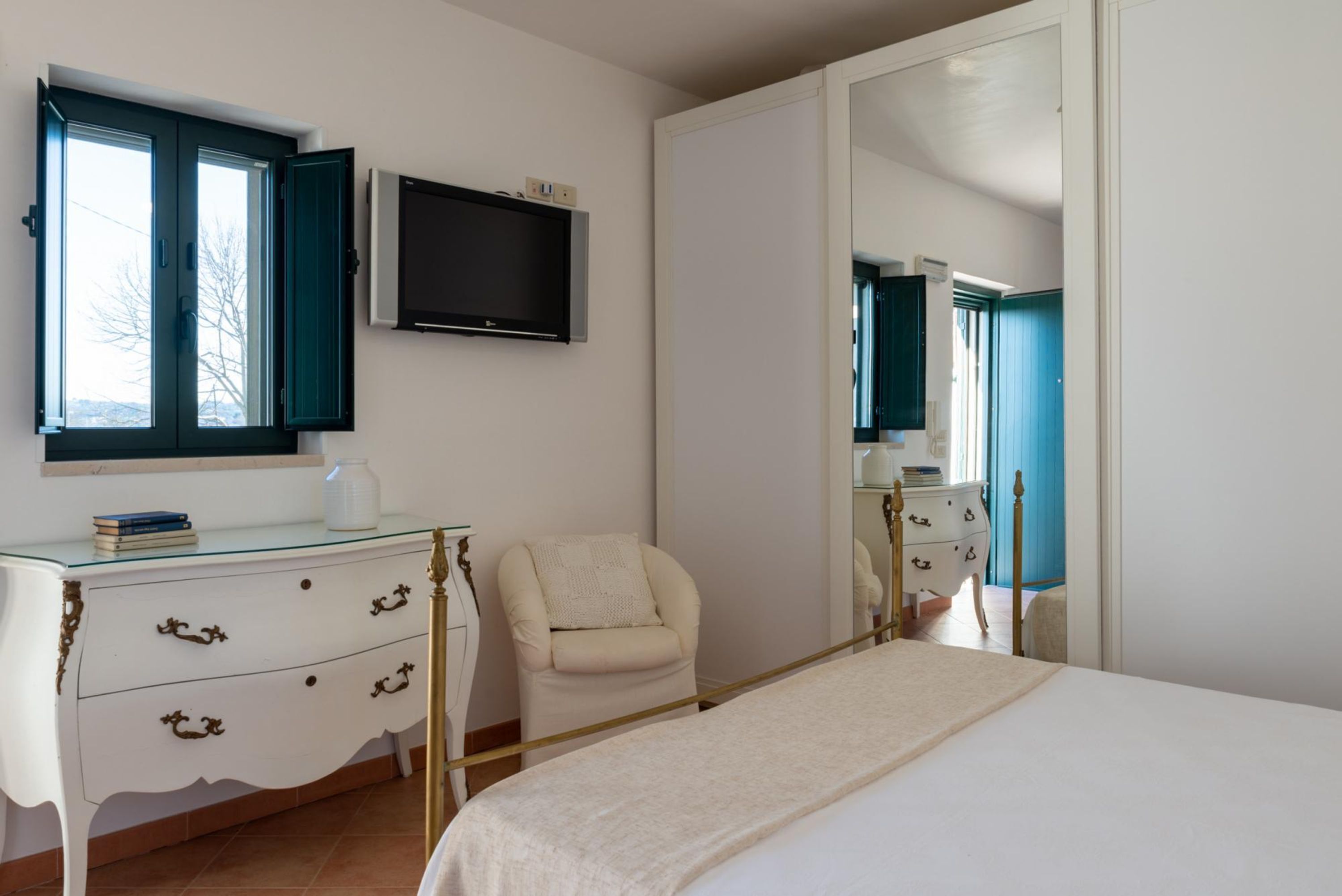 A bedroom with a bed, a dresser, a chair, a television, and a large mirror.