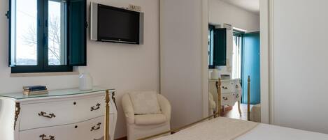 A bedroom with a bed, a dresser, a chair, a television, and a large mirror.