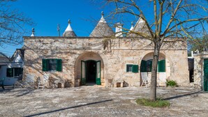 A stone building with arched doorways and green shutters, a paved courtyard, and a tree in the foreground. - Stile e Relax nei Trulli by Wonderful Italy (Martina Franca)