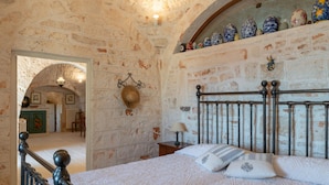 A bedroom with a stone wall, a bed with white bedding, and a nightstand with a lamp. - Stile e Relax nei Trulli by Wonderful Italy (Martina Franca)