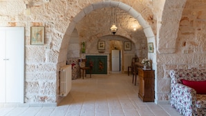 A stone-walled hallway with a door at the end, a radiator, and a chair with a floral pattern. - Stile e Relax nei Trulli by Wonderful Italy (Martina Franca)