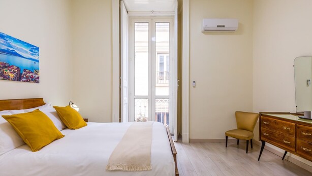 Une chambre d’hôtel avec un lit, une chaise, une commode et une fenêtre donnant sur des immeubles.