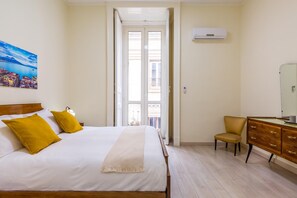 Camera d'albergo con un letto, una sedia, una cassettiera e una finestra vista edifici.