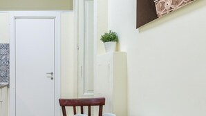 Une cuisine étroite avec une table à manger pour quatre personnes, une porte blanche et une petite plante en pot posée sur une étagère.