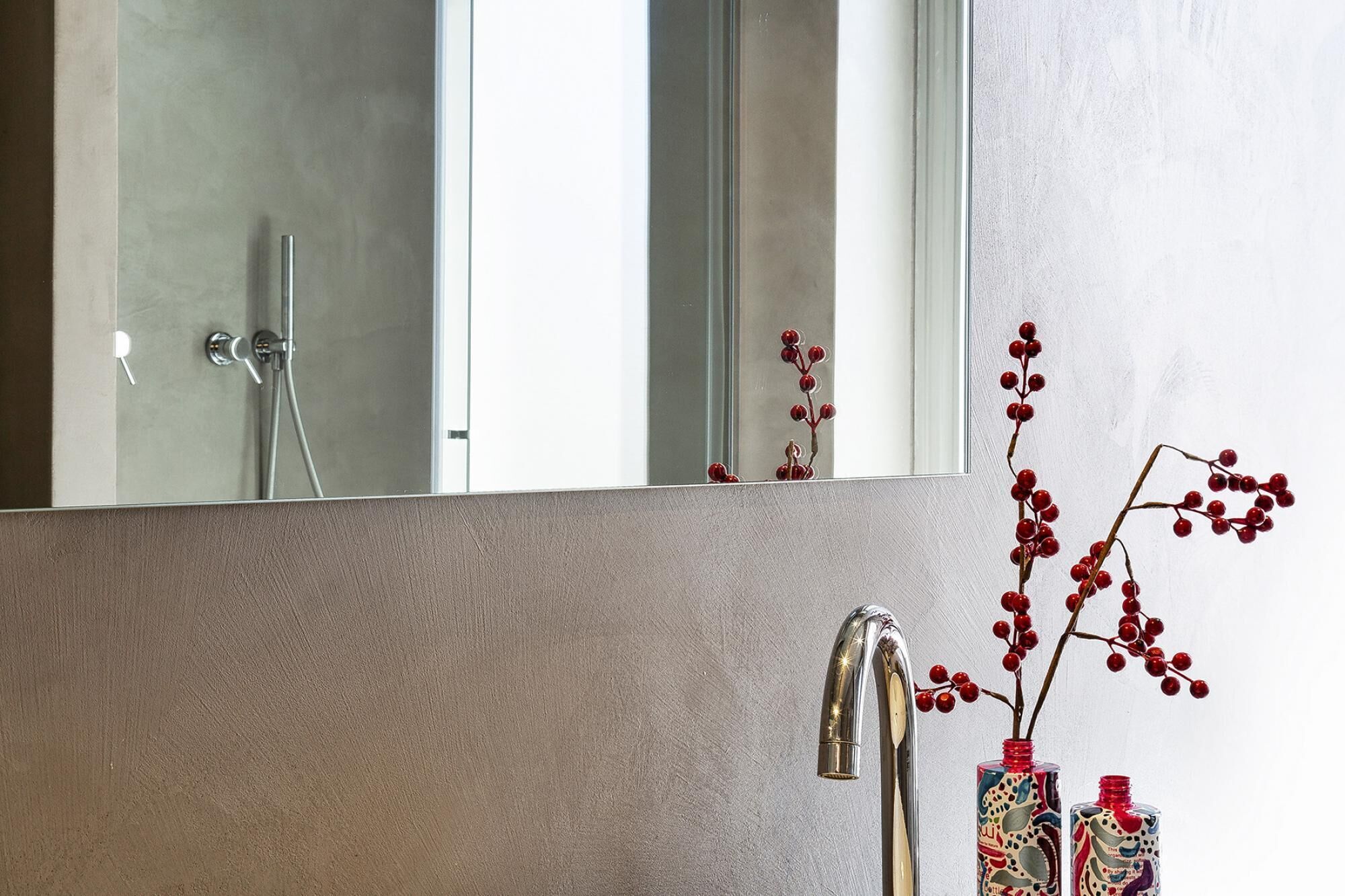 A bathroom with a large mirror, a modern faucet, and decorative red berries in a vase.