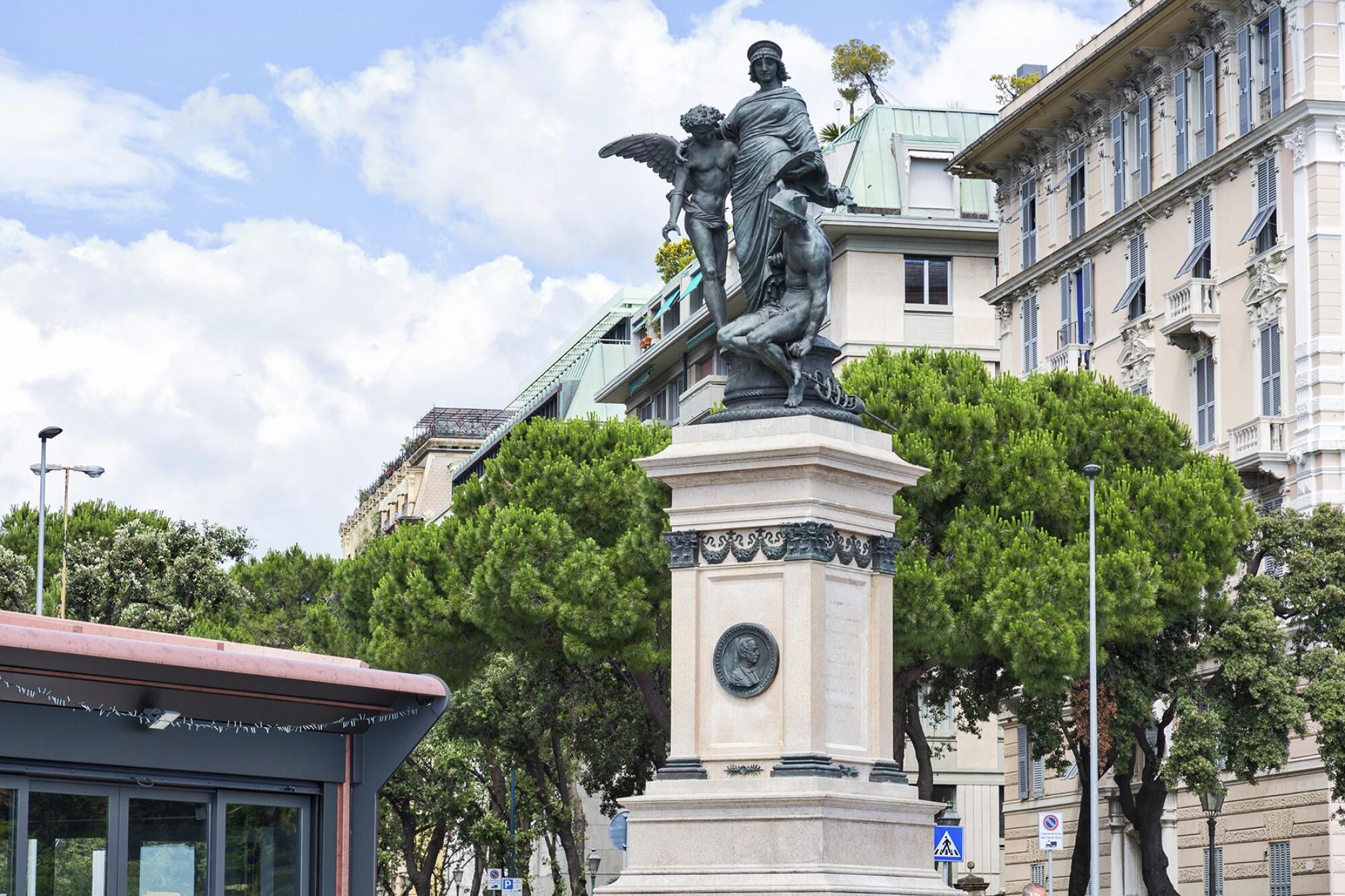 Una statua di un uomo con un angelo su un piedistallo, circondata da alberi ed edifici.