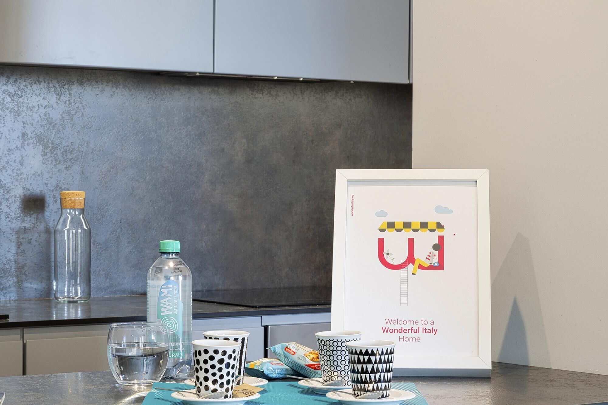 A kitchen counter with a framed picture of a colorful illustration, a bottle of water, and a glass.