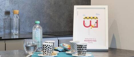 A kitchen counter with a framed picture of a colorful illustration, a bottle of water, and a glass.