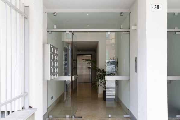 Une entrée d’hôtel moderne avec une porte en verre, un ascenseur bien visible et une plante en pot.