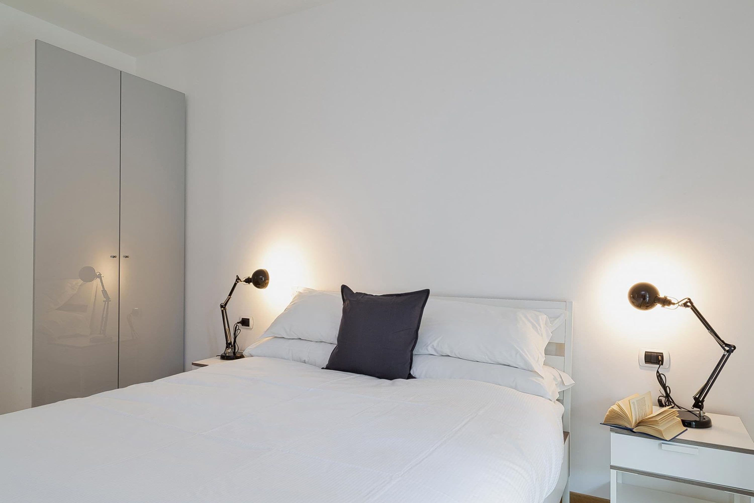 A neatly made bed with white linens, two bedside lamps, and a book on the nightstand.