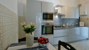 Une cuisine moderne équipée d’appareils électroménagers en acier inoxydable, une table à manger agrémentée d’un vase de fleurs et d’un saladier rempli de pommes.